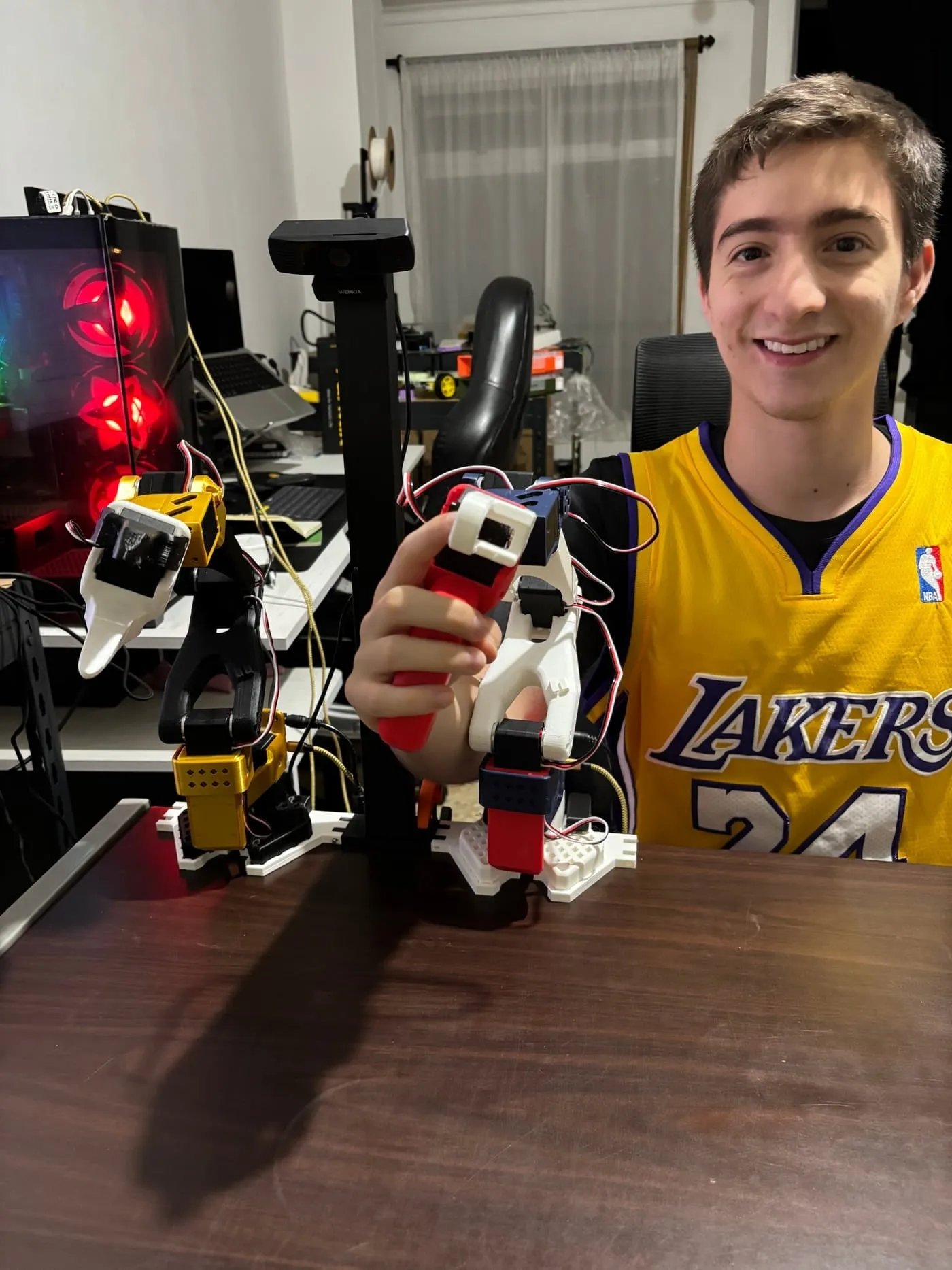 Juan Manuel Young Hoyos holding the leader arm of his two SO-100 robot arms, with the follower arm beside it